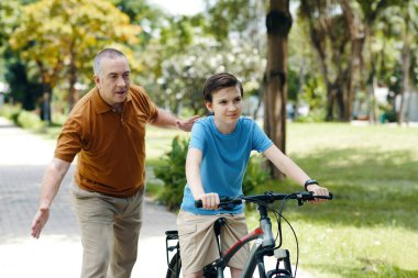 Büyükbaba torununa parkta yürürken bisiklet sürmeyi öğretiyor.