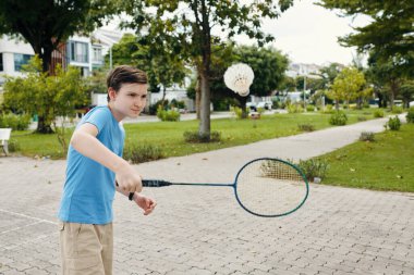 Raket tutan ve parkta badminton oynayan bir çocuk.