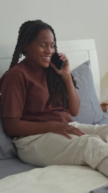 Afro-Amerikan kadının yatak odasında dinlenirken en iyi arkadaşıyla telefonda konuştuğu dikey çekim.