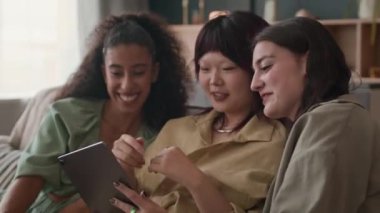 Evde toplanma sırasında kanepede otururken dijital tablet izleyen neşeli kadın zoomerların orta boy görüntüsü.
