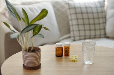 Evdeki odanın masasında bir şişe ilaç ve bir bardak su var.