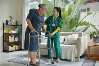 Sosyal hizmetler görevlisi evdeki yaşlı kadını umursuyor, yürümesine yardım ediyor.