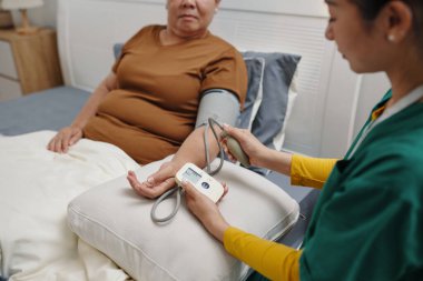 Bakıcı evde yatakta yatarken yaşlı kadının baskısını kontrol ediyor.