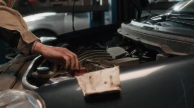 Beyaz erkek, üniforma uzmanı, atölyede çalışırken araba kaputunu kontrol ediyor.