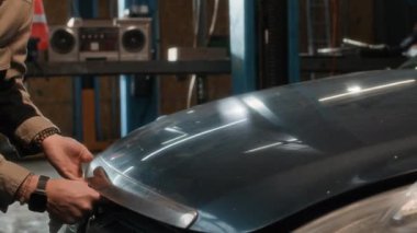 Garajında çalışırken, araba kaputunu aletlerle inceleyen beyaz tenli genç bir adamın el kamerası görüntüsü.