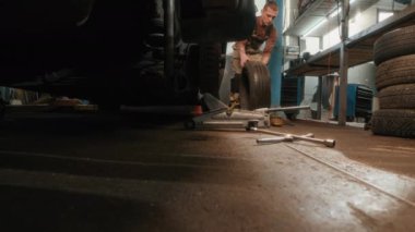 Erkek tamircinin atölyede çalışırken arabanın lastiklerini değiştirmesi düşük açılı bir bakış açısı.