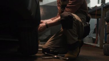 Otomobil atölyesinde çalışırken, üniformalı bir tamircinin kırık tekerleği çıkarırken görüntüsü kesilmiş.