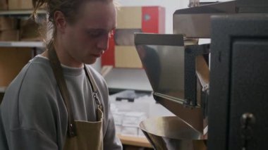 Beyaz önlüklü genç erkek işçinin roastery üretimindeki kahve poşetlerini paketleyip mühürlediği görüntüler.