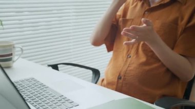 Hamile Asyalı yöneticinin ofis masasında dizüstü bilgisayarla iletişim kurarken cep telefonuyla yaptığı günlük kıyafet aramasını yukarı kaldır.