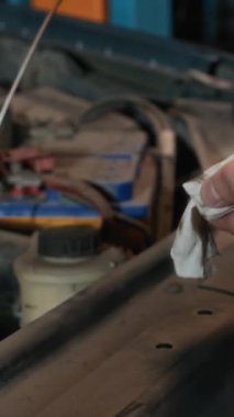 Otomobilin motor yağı seviyesini incelemek için dipstick kullanan isimsiz bir uzmanın dikey görüntüsü.