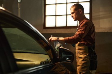 Araba servisindeki arabanın ön camını parlatmak için sprey kullanan bir işçi.