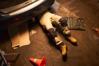 Yüksek açılı tamirci yerde yatıyor ve arabayı garajda inceliyor.