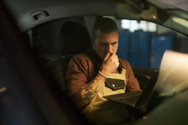 Tamirci araba kuaföründe otururken arabayı dizüstü bilgisayarla inceliyor.