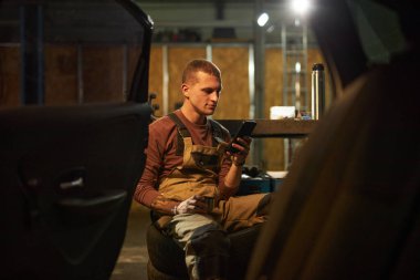 Kahve molasında tamirci oturuyor ve akıllı telefon kullanıyor.