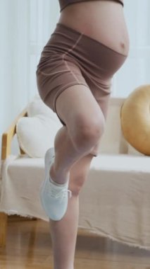 Aktif giyimli hamile bir kadının evde egzersiz yaparken yoga çalışmasının dikey çekimi.