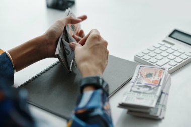 Yüksek açılı, tanınmayan kadın banka çalışanı elleri ofiste otururken para sayıyor.