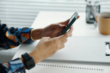 Ofisteki uygulamayı kullanarak akıllı telefon tutan tanınmayan genç bir ofis çalışanının elleri.