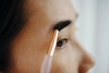 Jel sürdükten sonra kaşlarını fırçalarken makyaj yapan Asyalı genç kadının aşırı yakın çekimi.