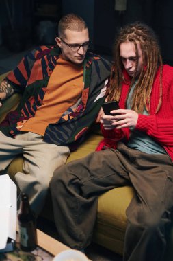 Ev partisi sırasında kanepede oturup akıllı telefondan video oyunu oynayan adamlar.