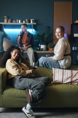 Mutlu gençlerin portresi kanepede oturup kameraya gülümsüyor ve ev partisinde buluşuyorlar.