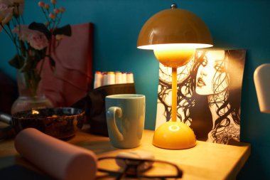 Drawing of young woman and lamp with warm light on cluttered table in dimly lit gen Z girls dorm room clipart