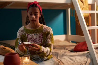 Yaratıcı nesil Z kızı yurt odasında rahat bir atmosfer yaratıyor, mumları yakıyor.