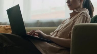 Kafkasyalı iş kadınının ev ofisteki koltukta otururken kablosuz laptopla haber yaptığı düşük açılı görüntü.