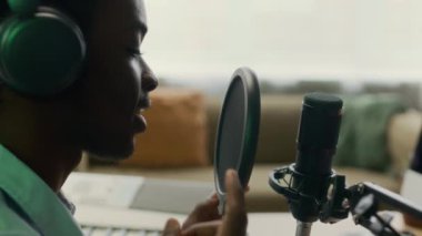 Kablosuz kulaklıklı genç bir erkek podcaster canlı yayında mikrofonla konuşuyor ve stüdyodaki takipçilerle konuşuyor.