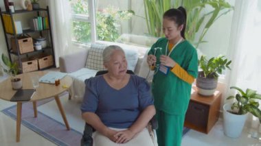 Ev ziyareti sırasında steteskop kullanarak yaşlı hastaların ciğerlerini kontrol eden tıbbi önlük giyen Asyalı genç bayan sosyal hizmet görevlisinin görüntüsü