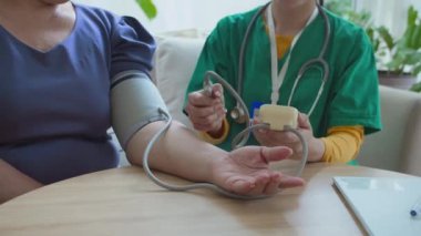 Bilinmeyen yaşlı bir kadının tansiyonunu ölçmek için elektronik sfenometre kullanan, ameliyat önlüklü, tanınmayan bir tıp çalışanının orta bölüm fotoğrafı.