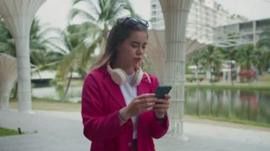 Şehirde yürürken kablosuz kulaklık takan, akıllı telefonlardan sohbet eden kadın çok ırklı zoomer 'ın orta boy fotoğrafı.