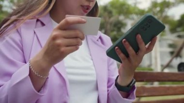 Kültürler arası genç bir kızın şehir parkında internet üzerinden ödeme yaparken kredi kartı kullanmasının düşük açılı görüntüsü.