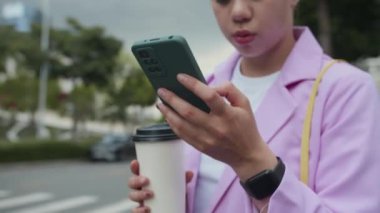 Şehir caddesinde taksi çağırmak için akıllı telefondaki uygulamayı kullanarak çok ırklı kadın zoomerı bir fincan kahveyle yukarı kaldır.