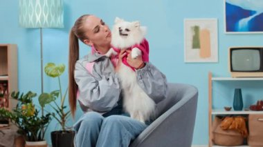 Beyaz tüylü, 90 'lı mobilyalı oturma odasında dinlenirken beyaz tüylü bir köpeği okşayan Kafkas kökenli Y jenerasyonundan bir kadın.