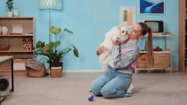 Haftasonunu mobilyalı oturma odasında birlikte geçirirken Y jenerasyonunda mutlu bir kadının tatlı tüylü bir köpeği oynaması ve okşaması.