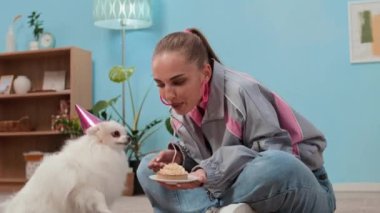 Beyaz tüylü sevimli köpeğe doğum günü ziyafeti veren genç beyaz bir kadının eski moda oturma odasında el kamerasıyla çekilmiş fotoğrafı.