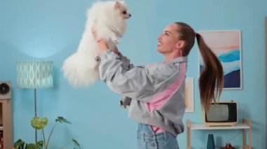 90 'lı yılların moda kıyafetleri ve halka küpeleriyle beyaz pomeranian tarzıyla retro dairede oynayan neşeli beyaz kadın.