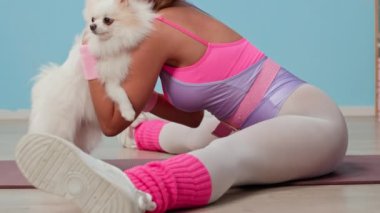 Pembe ve mor 80 'ler spor kıyafetleriyle beyaz kadın sporcunun pofuduk Pomeranya' lıya sarılıp bacak ayrımında otururken kameraya gülümseyen yavaş yavaş portresini kaldır.