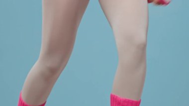 Pembe ve mor 80 'ler spor kıyafetleri ve ayak ısıtıcıları giymiş beyaz kadın sporcunun küçük dambılları elinde tutarken ayak egzersizleri yaptığı sahneleri yukarı kaldırın.