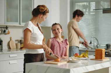 Üç kişilik mutlu bir aile mutfakta birlikte yemek pişiriyor.