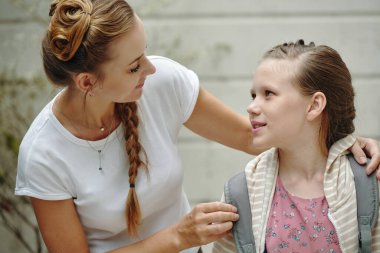 Anne kızına okul çantası giymesi için yardım ediyor ve onu okula hazırlıyor.