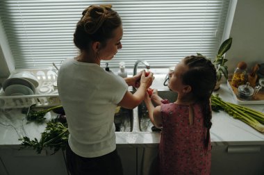 Anne ve kızının mutfakta birlikte taze sebze yıkarkenki görüntüsü.