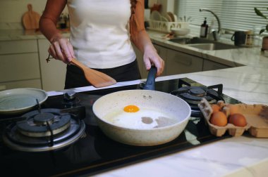 Ev hanımı kahvaltıda tavada yumurta pişiriyor.
