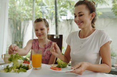 Anne ve kızı evdeki yemek masasında birlikte kahvaltı ediyorlar.