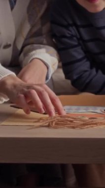 Kafkasyalı neşeli bir çocuğun ebeveyni oturma odasında masa başında kağıt işçiliği yaparken dikey pozu.