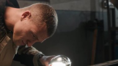 Atölyede bozulma sebebini incelerken el feneri kullanan beyaz erkek tamircinin el kamerasıyla çekilmiş resmi.