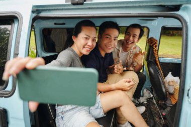 Minibüste arkadaşlarıyla cep telefonunda selfie çeken mutlu bir kız.