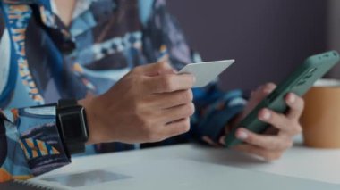 Ofisteki akıllı telefondan ödeme yaparken elinde kredi kartı tutan isimsiz bir iş kadınının el kesimi.