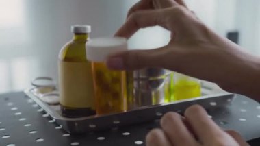 Kapalı alandaki ilaçlı tepsideki vitaminlerle şişeyi alan anonim kişinin ellerini yakın çekimde çek.