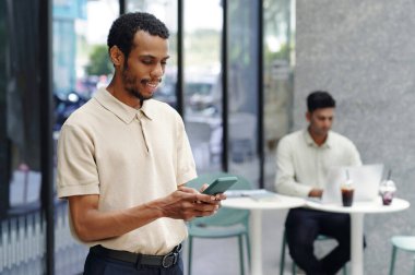 Gülümseyen işadamı modern ofiste çalışırken cep telefonundan mesaj atıyor.